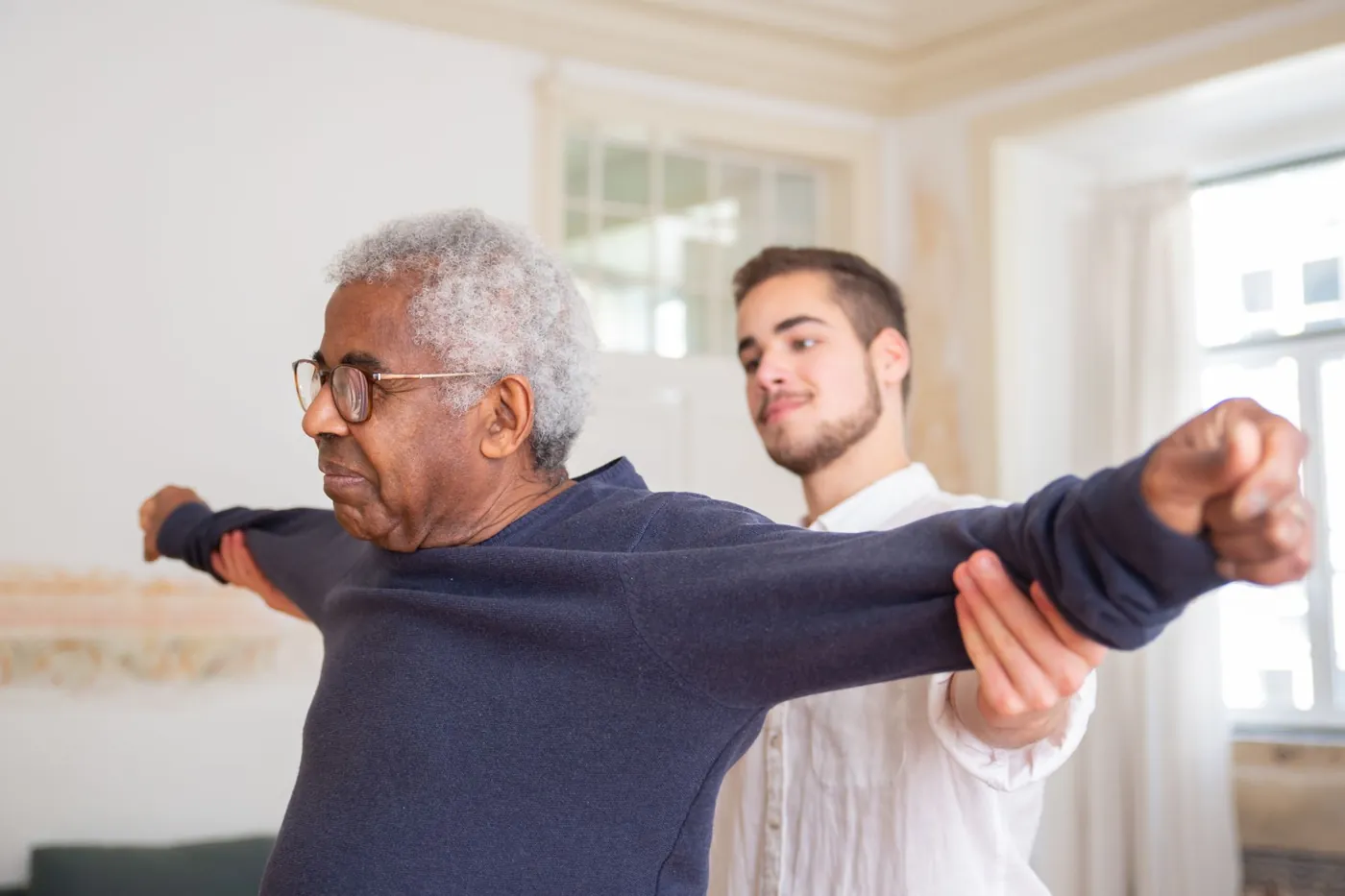 An older man doing a gentle seated stretch with a helper beside him