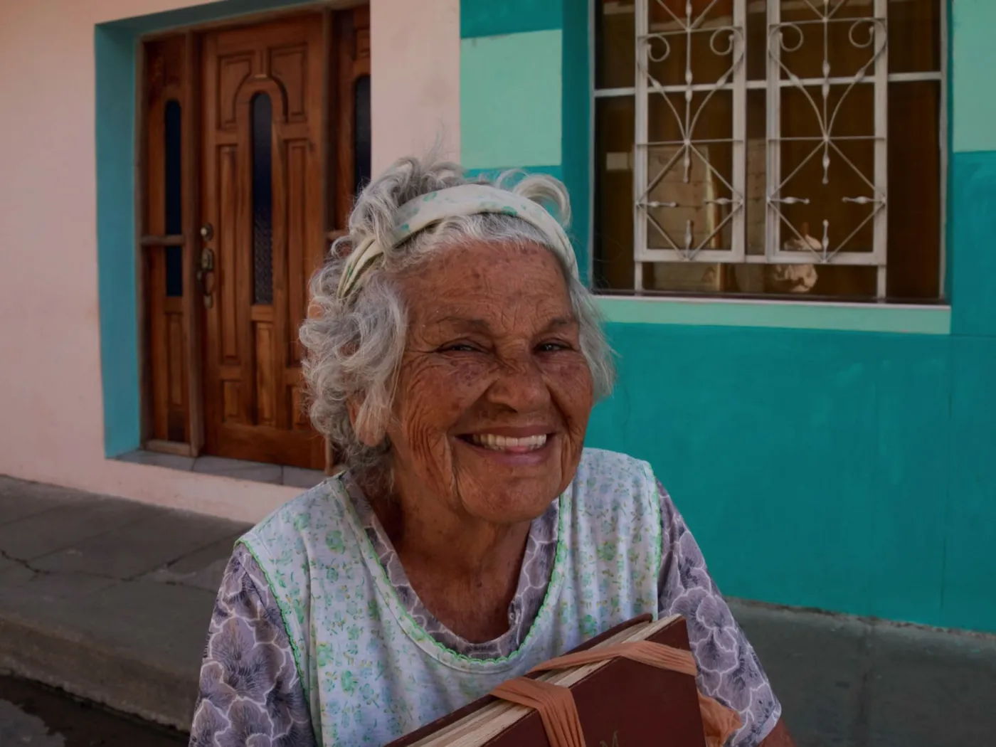 A smiling older woman outside her colorful front door