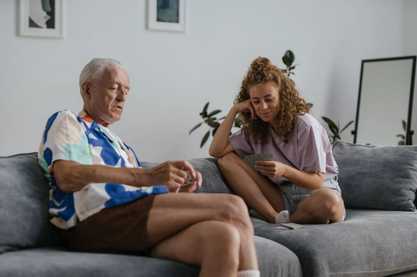 An older man and a younger woman sharing a card game on the sofa