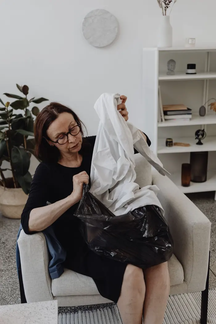 A woman sorting linens into a bag while seated in a light, tidy living room