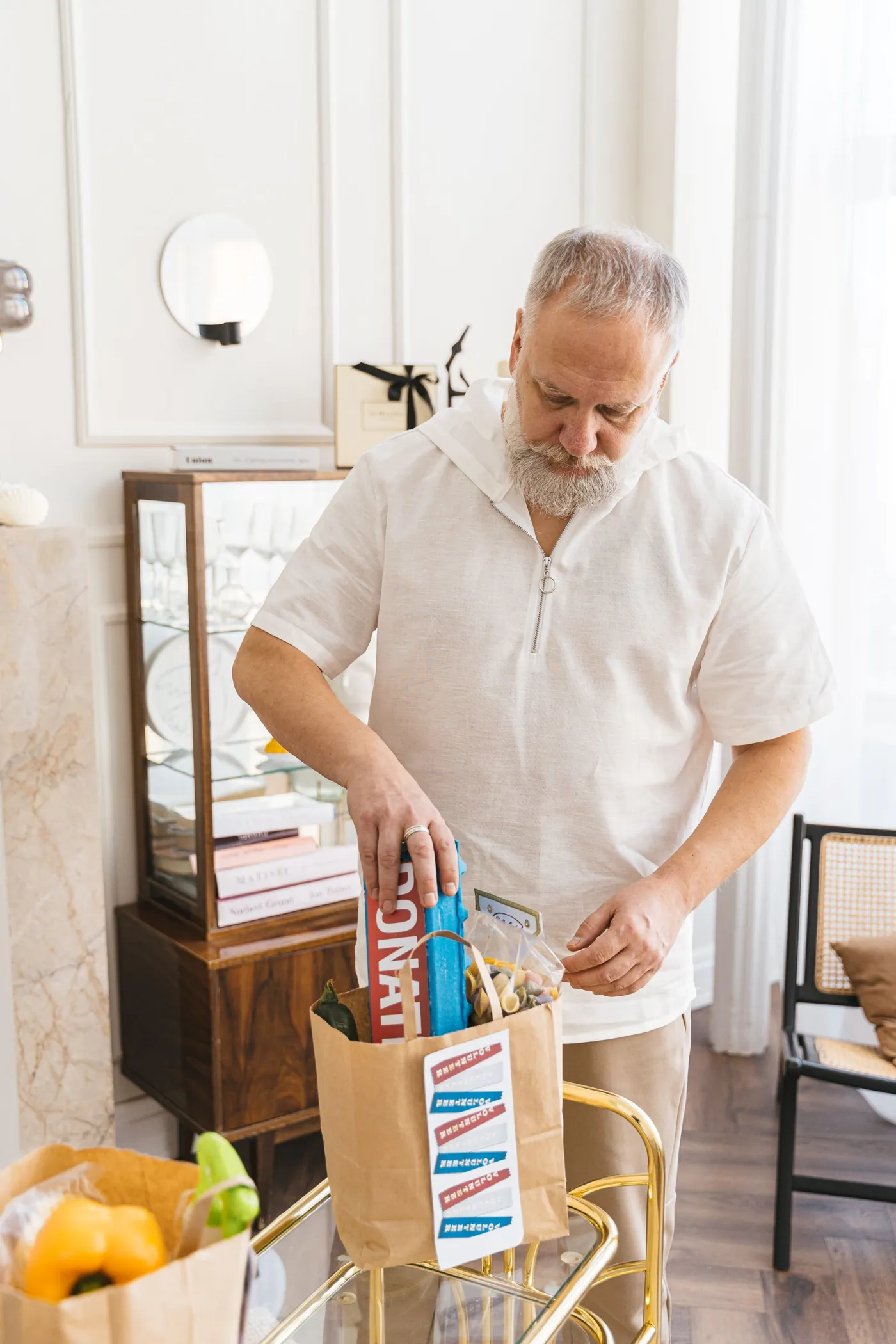 An older man unpacking a bag of groceries on a serving cart at home